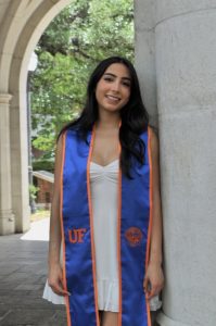 Emily in an outdoor archway wearing a white dress and blue graduation sash, Hispanic food | Food Science and Human Nutrition UF/IFAS