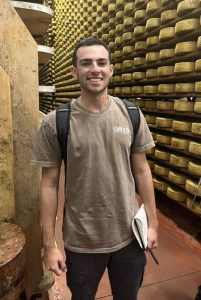 Zachary Howard standing in a cheese cave in front of a large number of cheese wheels | Food Science and Human Nutrition UF/IFAS