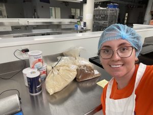 Melissa wearing a red shirt and blue cap with lab materials on a table behind her, facial pain | Food Science and Human Nutrition UF/IFAS