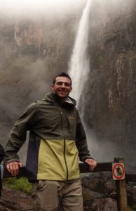 Zachary wearing a jacket and standing in front of a waterfall.