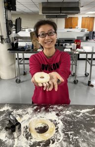 Woman holding up a ring of donut dough.