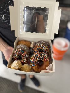 Hands holding a white box filled with donuts.