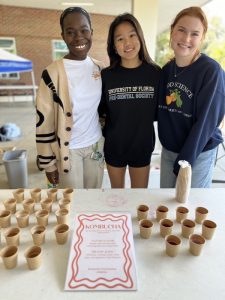 Three students standing behind a table outside with small cups of kombucha on the table in front of them, food | Food Science and Human Nutrition UF/IFAS