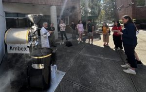 A line of people watching a coffee-roasting demonstration outside a large building.