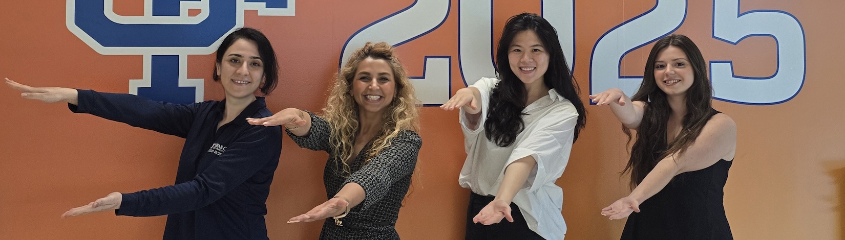 Dr. Farzad and three graduate students doing the Gator Chomp in front of an orange wall.