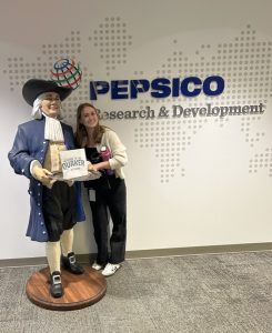 Evelyn standing with a statue of the Quaker Oats character in front of a PepsiCo sign.