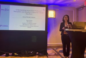 Rose in a dark suit presenting at a podium with a large screen behind her, cell-based seafood | Food Science and Human Nutrition UF/IFAS