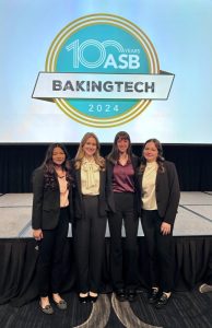 Four women in dark suit stand in front of a projector screen with the BakingTECH logo, opportunity | Food Science and Human Nutrition UF/IFAS
