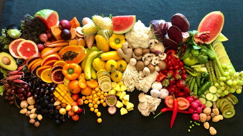 A colorful array of fruits and vegetables arranged on a dark table, gut health.