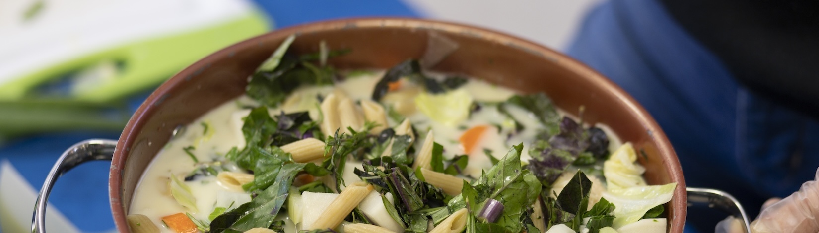 Cropped image of a vegetable and pasta soup in a brown bowl.