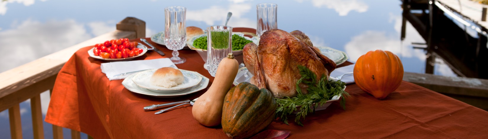 A fall food spread including a turkey and several varieties of squash on a lakeside table.
