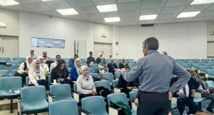 A professional gathering in a lecture hall with a male speaker addressing seated attendees.