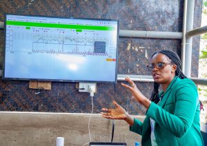 A presenter gestures while explaining livestock sensor data displayed on a monitor