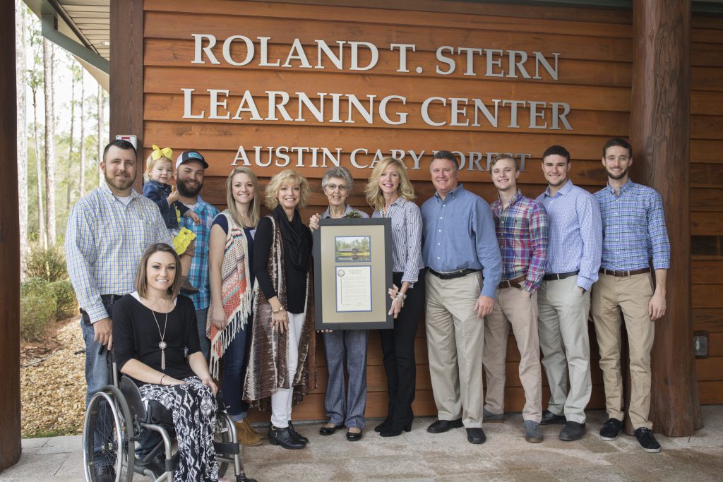 The Stern family outside the Roland T. Stern Learning Center. Lucinda and her daughters hold a framed certificate and photo.