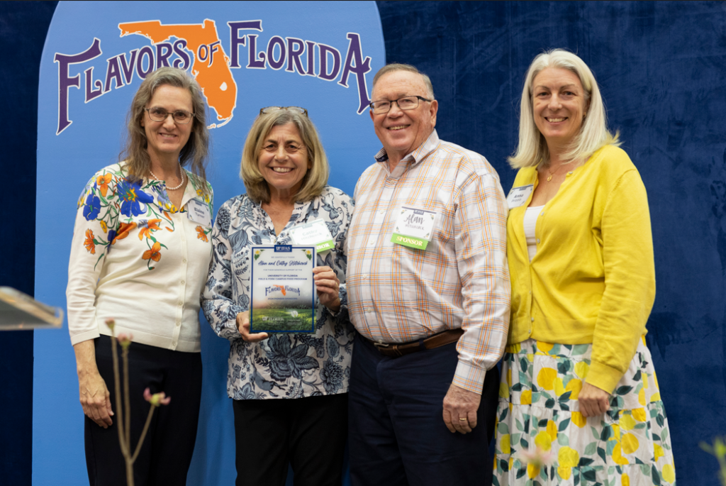 Elaine Turner, Cathy Hitchcock, Alan Hitchcock, and Anna Prizzia smile and pose on stage at the 2024 Flavors of Florida. Cathy holds a colorful plaque. The Flavors of Florida event logo is visible in the background.