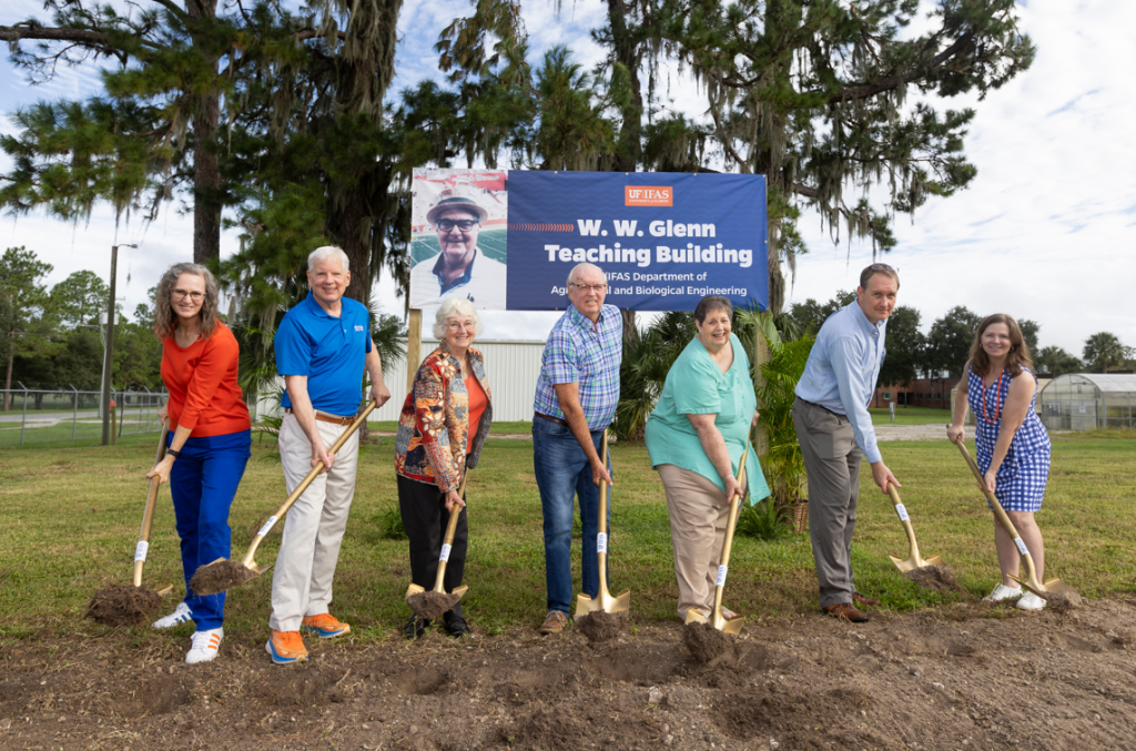 A line of people posing with shovels in front of a sign that reads "WW Glenn Teaching Building."