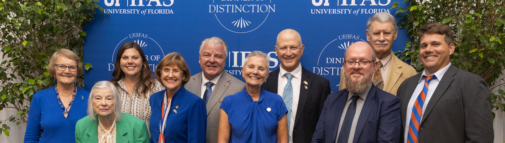A group of smiling people in business attire stand in front of a blue UF/IFAS Dinner of Distinction step-and-repeat backdrop