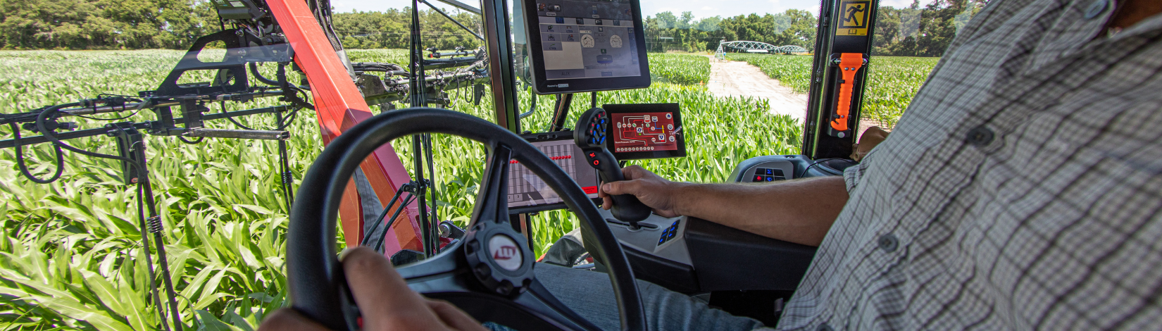 Trevor Ross driving an elevated tractor while applying fertilizer to a corn field.