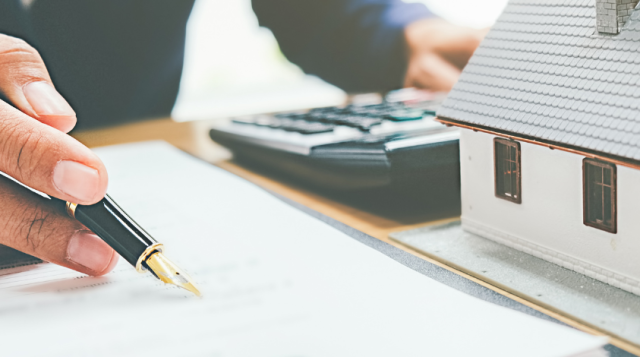 Hand with Pen writing and next to a model house