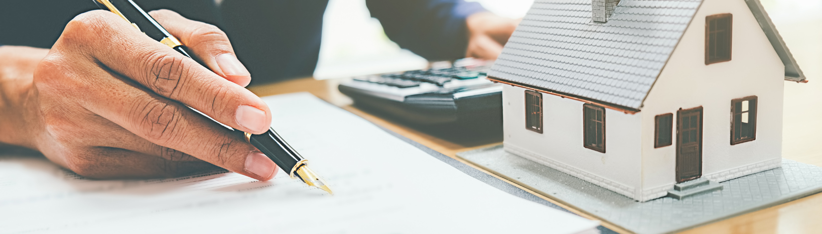 Hand with Pen writing and next to a model house