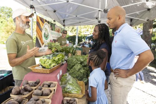 A family shopping for produce and talking to the owner of Frog Song Organics at a farmers market. Photo taken 09-13-21