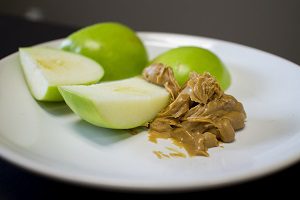 A cut green apple lies next to peanut butter on a plate.