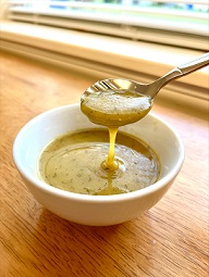 Freshly prepared honey-mustard salad dressing drizzled from a spoon into a bowl