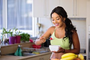 A woman smiles while eating a bowl of fruit. 