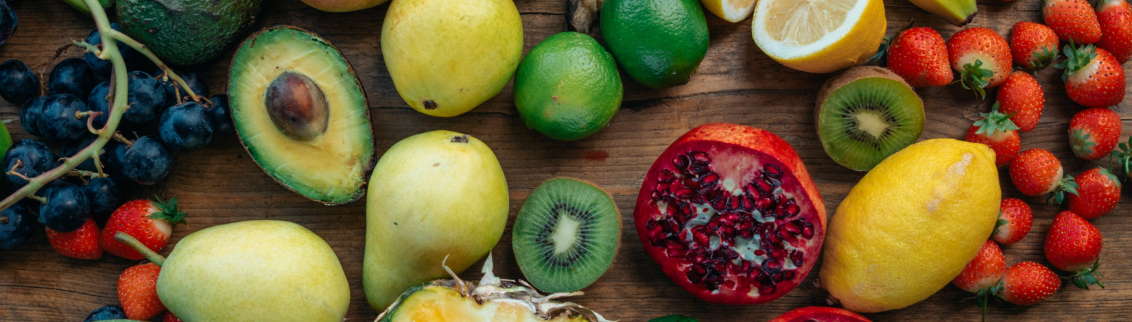 An array of colorful fruits and vegetables lay spread on a wooden table.