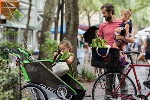 Father and young daughters loading their farmer's market produce into their bicycle trailer after shopping. UF/IFAS Photo Database.