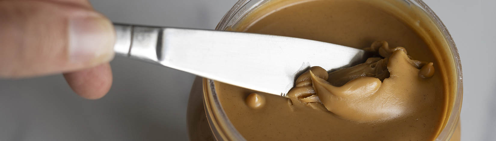 A shiny butter knife slides silkily through a freshly opened jar of smooth peanut butter.