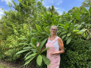 Mary Calo is shown next to a multi-species shrub border in her yard, including a blooming frangipani.