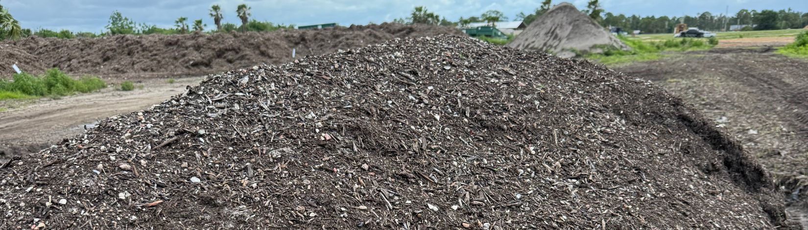Close-up of a compost pile, showing small pieces of organic matter in the process of decomposition. In the background are other compost piles in process.