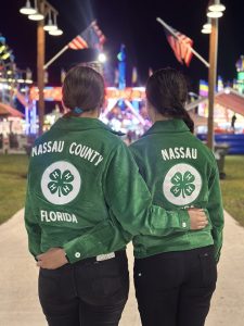 two 4-H members wearing green jackets in front of farris wheel at nigh