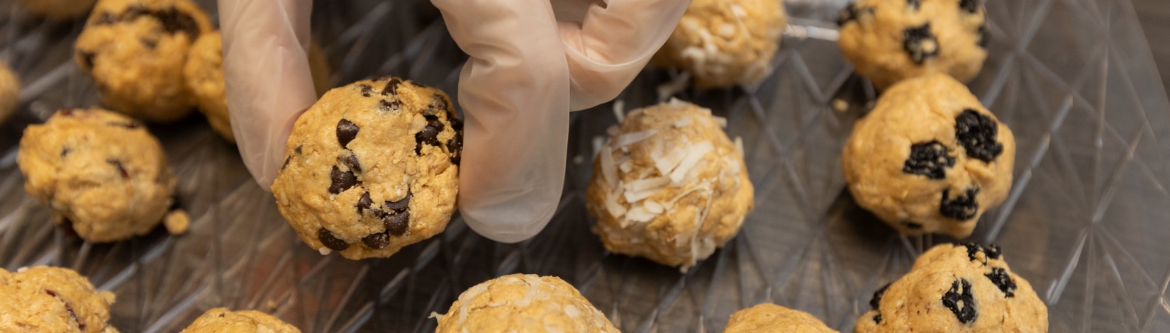 Gloved hand placing finished energy bites on a tray.
