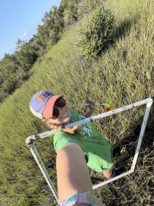 A selfie of Ella in the marsh carrying a quadrat.