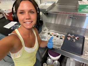 A selfie of Frankie the intern in the lab wearing heaphones and gloves while prepping stable isotope samples. 
