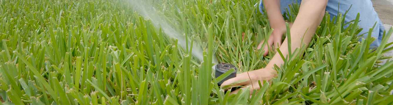 hand adjusting the direction of a sprinkler watering a lawn