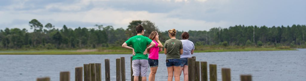 a group of students stand on the end of a dock on a lake