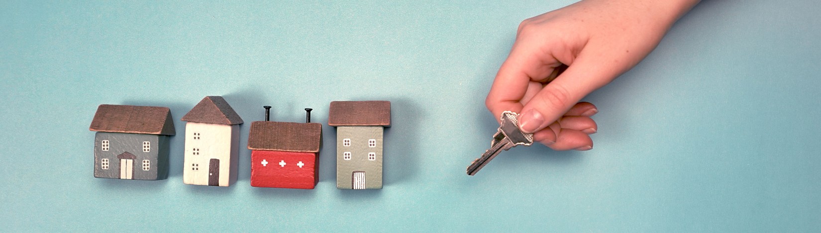 Key held by a hand with miniature wooden houses against a blue background