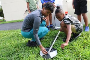 Pamela Aracena Santos with children in a grassy area, teaching students from the Muck City Angler summer program how to measure Secchi disk depth to assess water quality.
