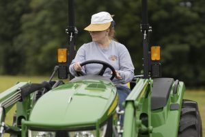 A woman wearing a cap driving a green tractor.