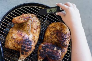 Using a meat thermometer to take the temperature of chicken on a grill. UF/IFAS Tyler Jones