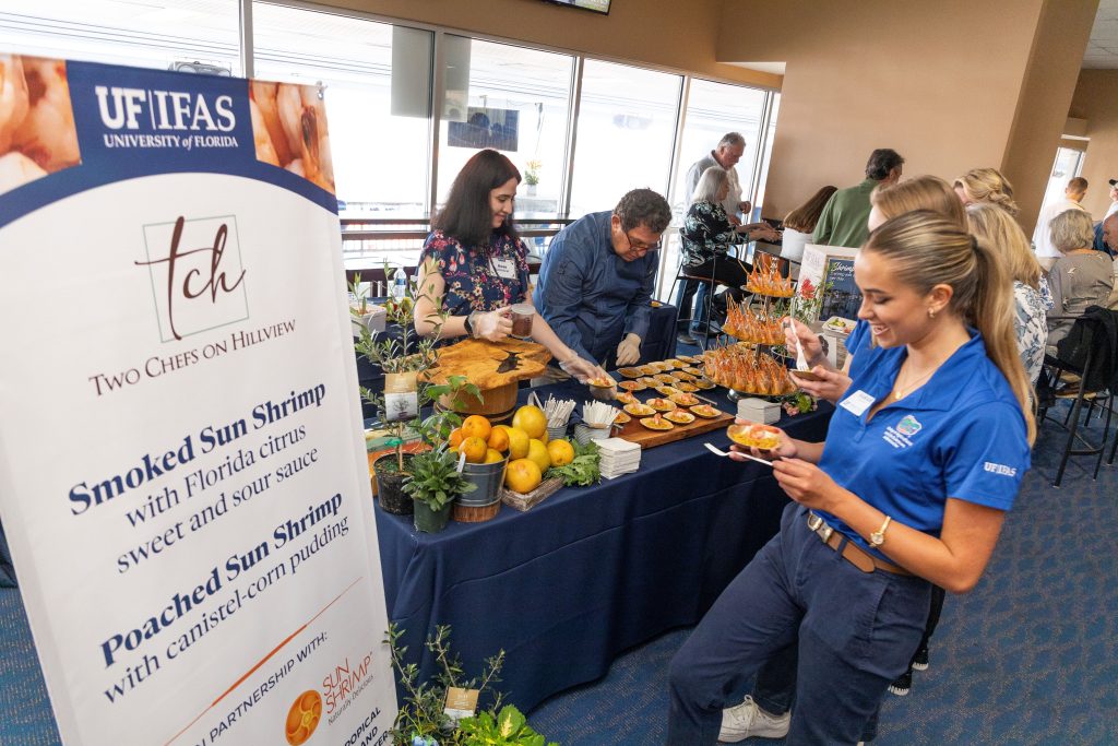 A woman picks up a dish of shrimp from a table.