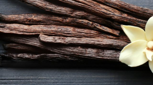 Dried vanilla sticks with a vanilla flower on a dark wooden background.