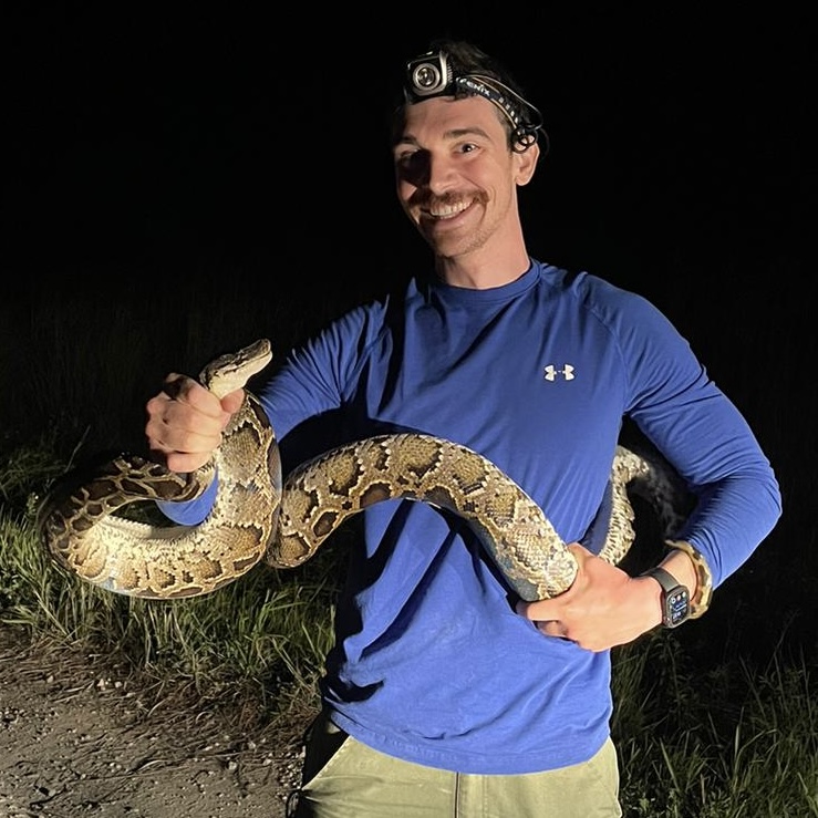Researcher Alex Romer holds a captured Burmese python during nighttime fieldwork in the Everglades.