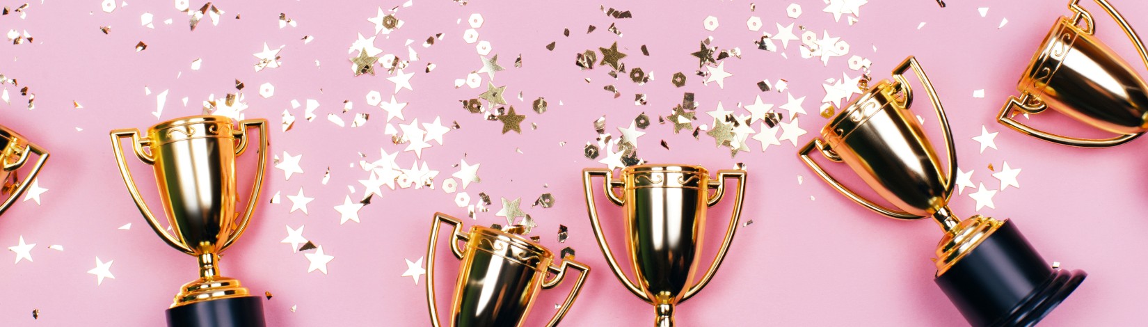 Golden winner cups with sparkles on a pink background with copy space. Festive concept. Flat lay style.