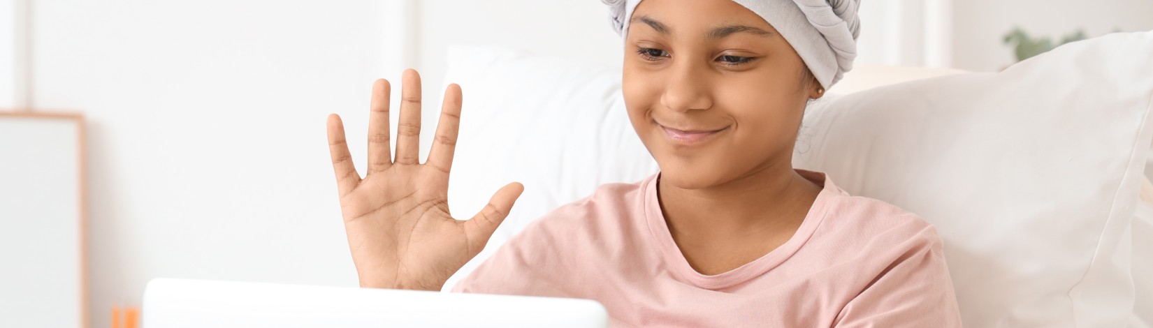 A girl with cancer waves at a computer.