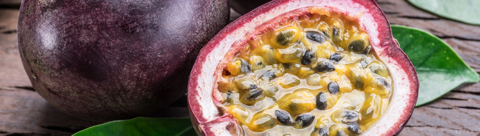 A passionfruit cut in half next to a whole passionfruit on a wooden surface