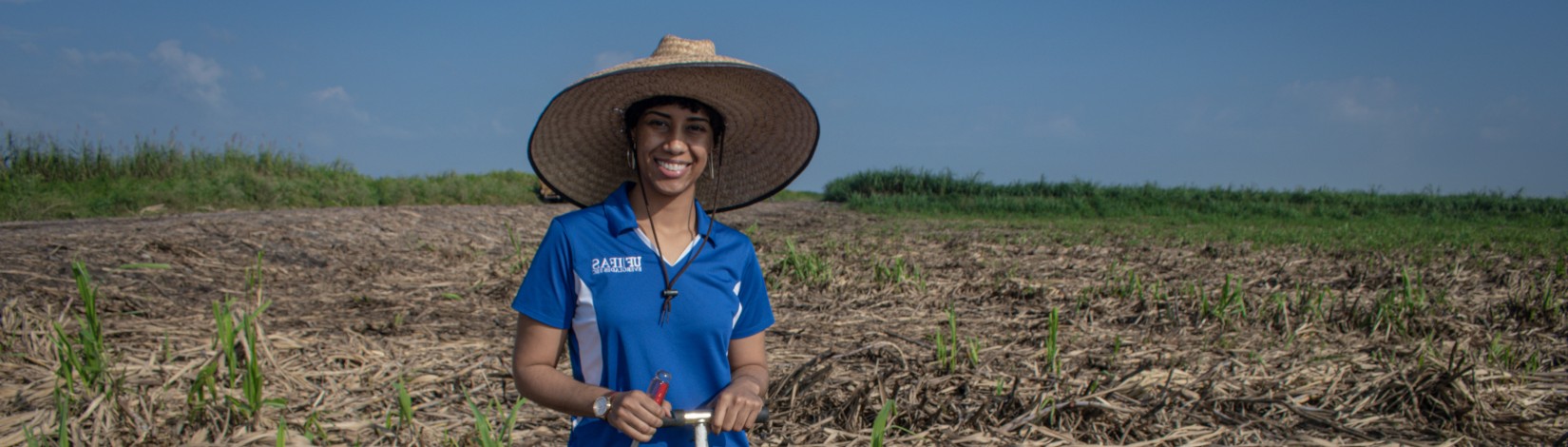 A women standing in front of a field, wearing a hat.